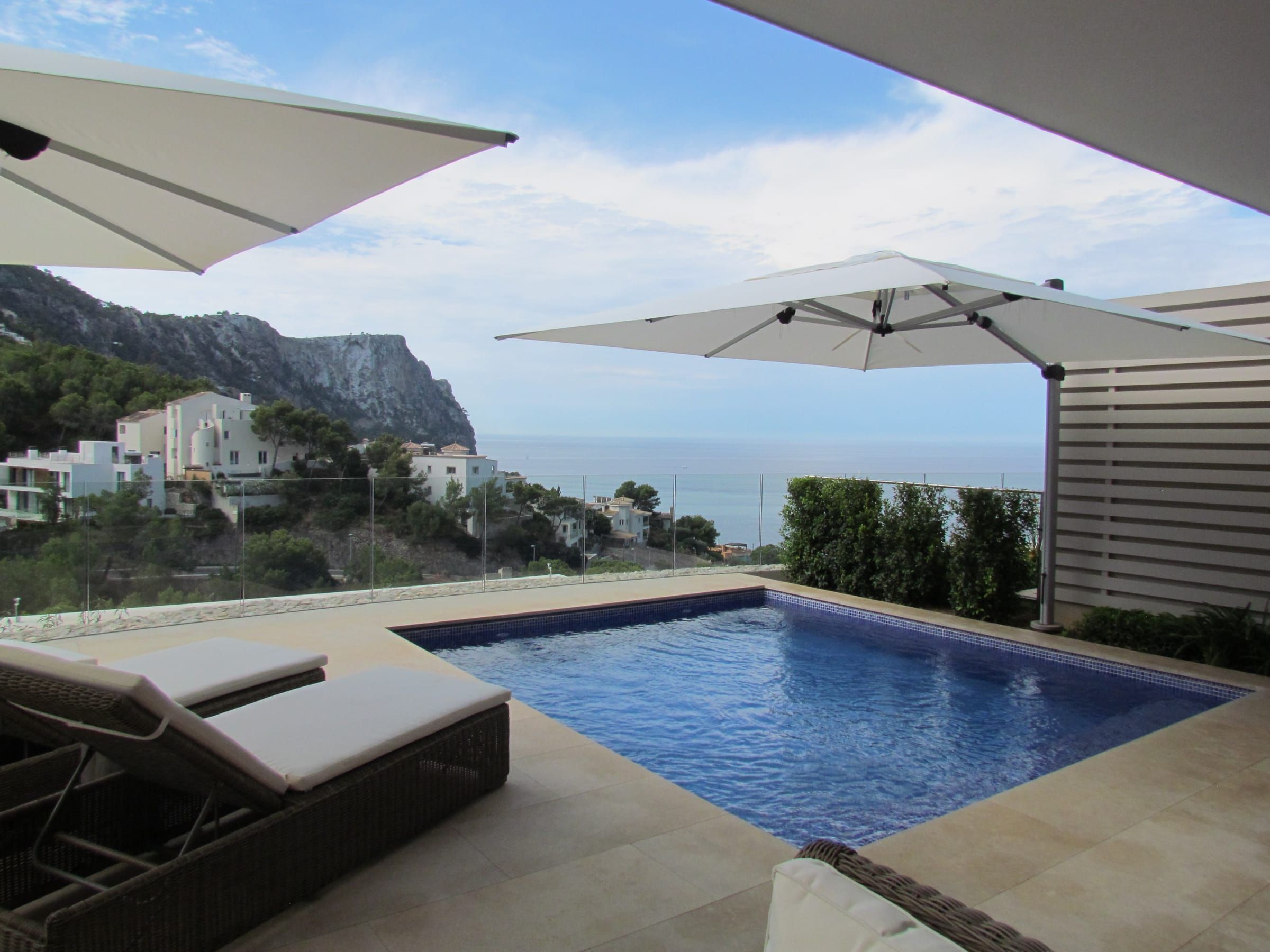 Two white parasols over the pool and sun loungers with sea views