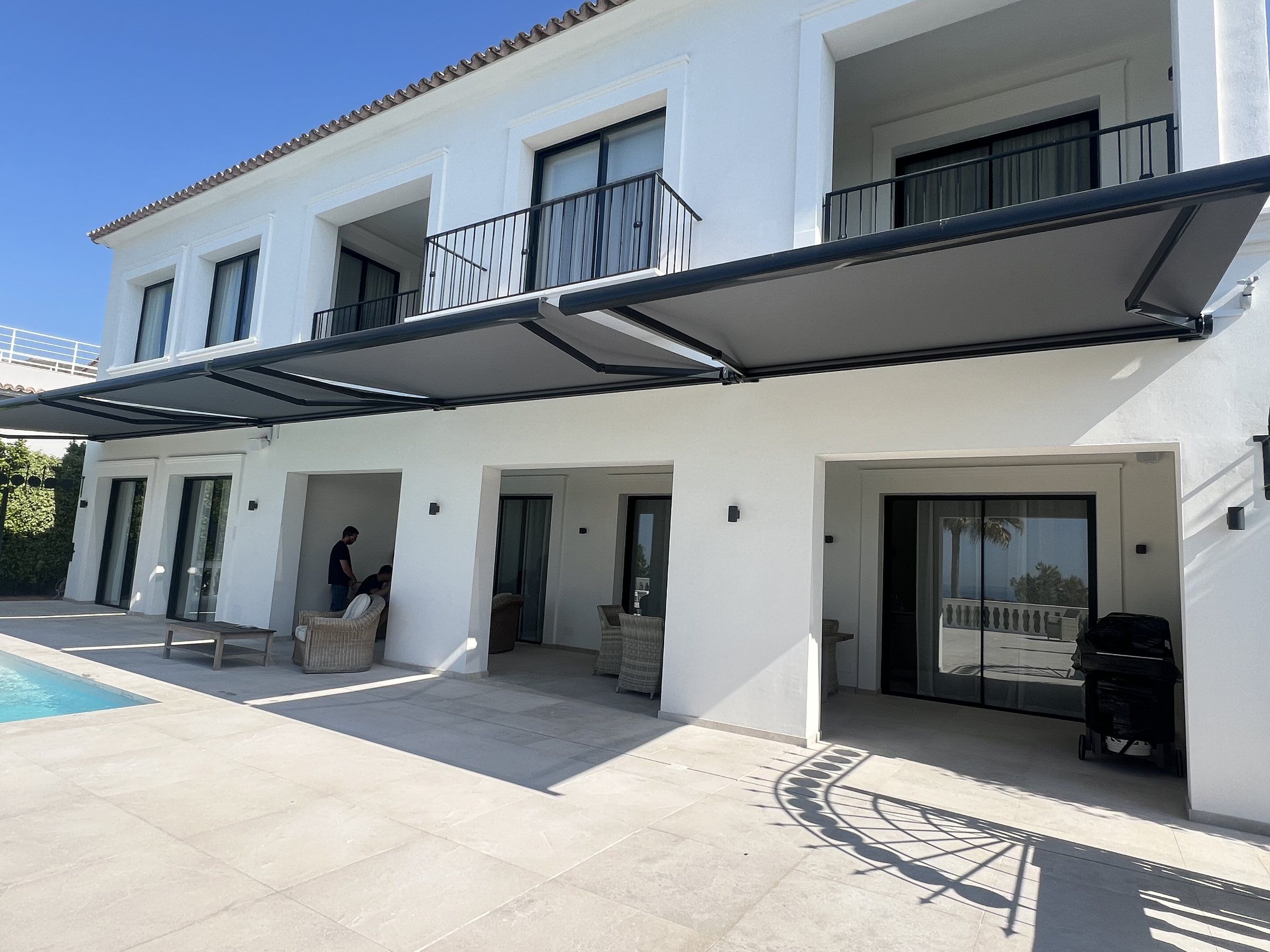 Toldo cofre gris extendido sobre la terraza junto a la piscina de una casa blanca