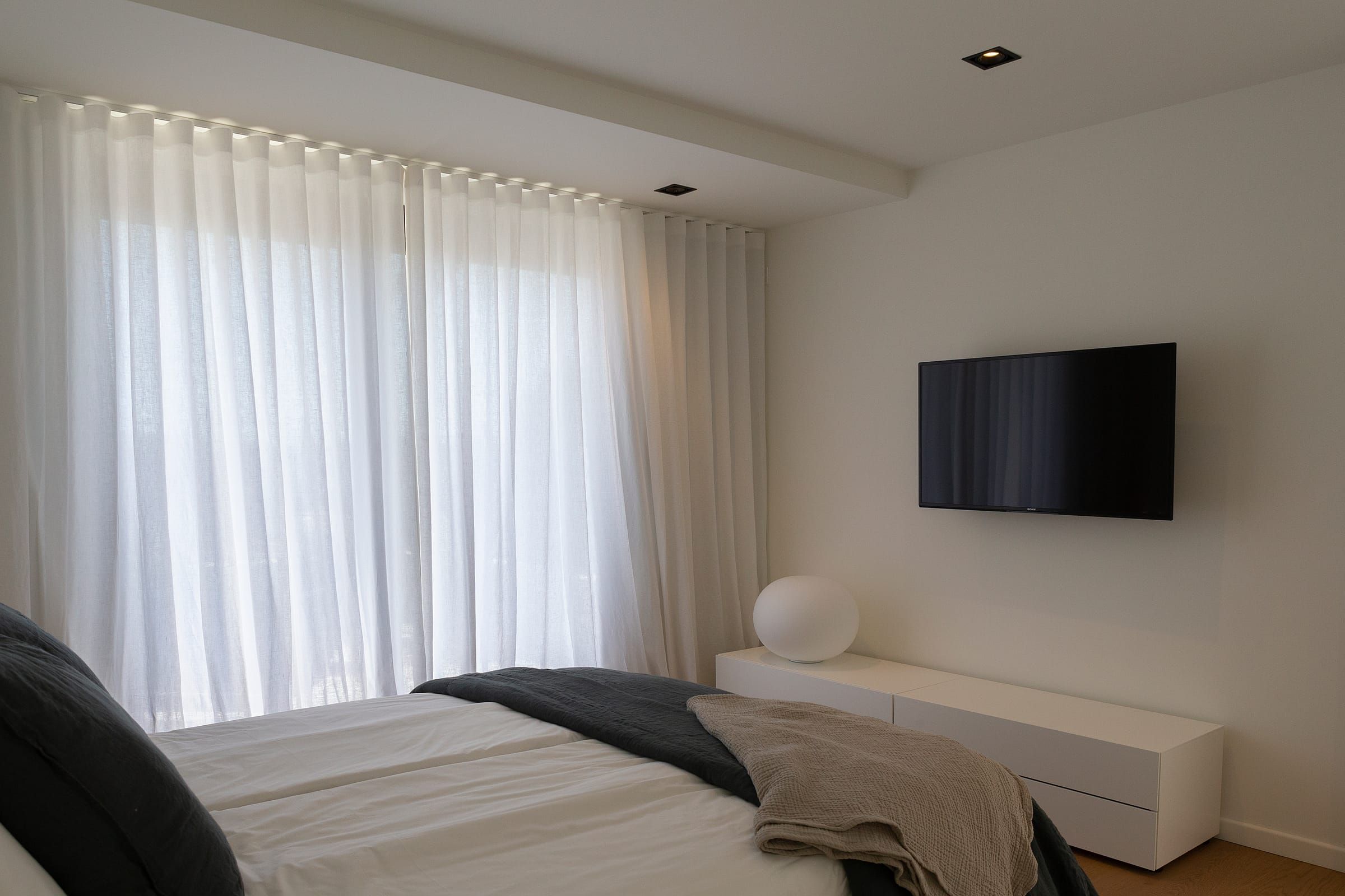 Schlafzimmer mit weißen Wellenvorhängen vor der großen Fensterfront