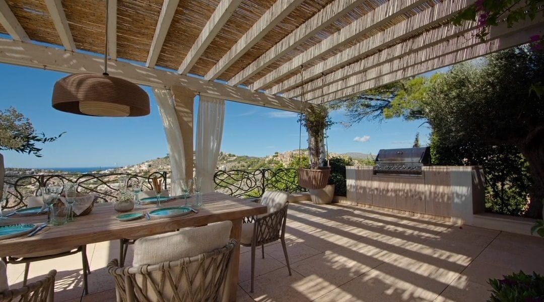 Essbereich und Sommerküche unter einer Schilfrohr-Pergola mit gerafften Außenvorhängen und Meerblick