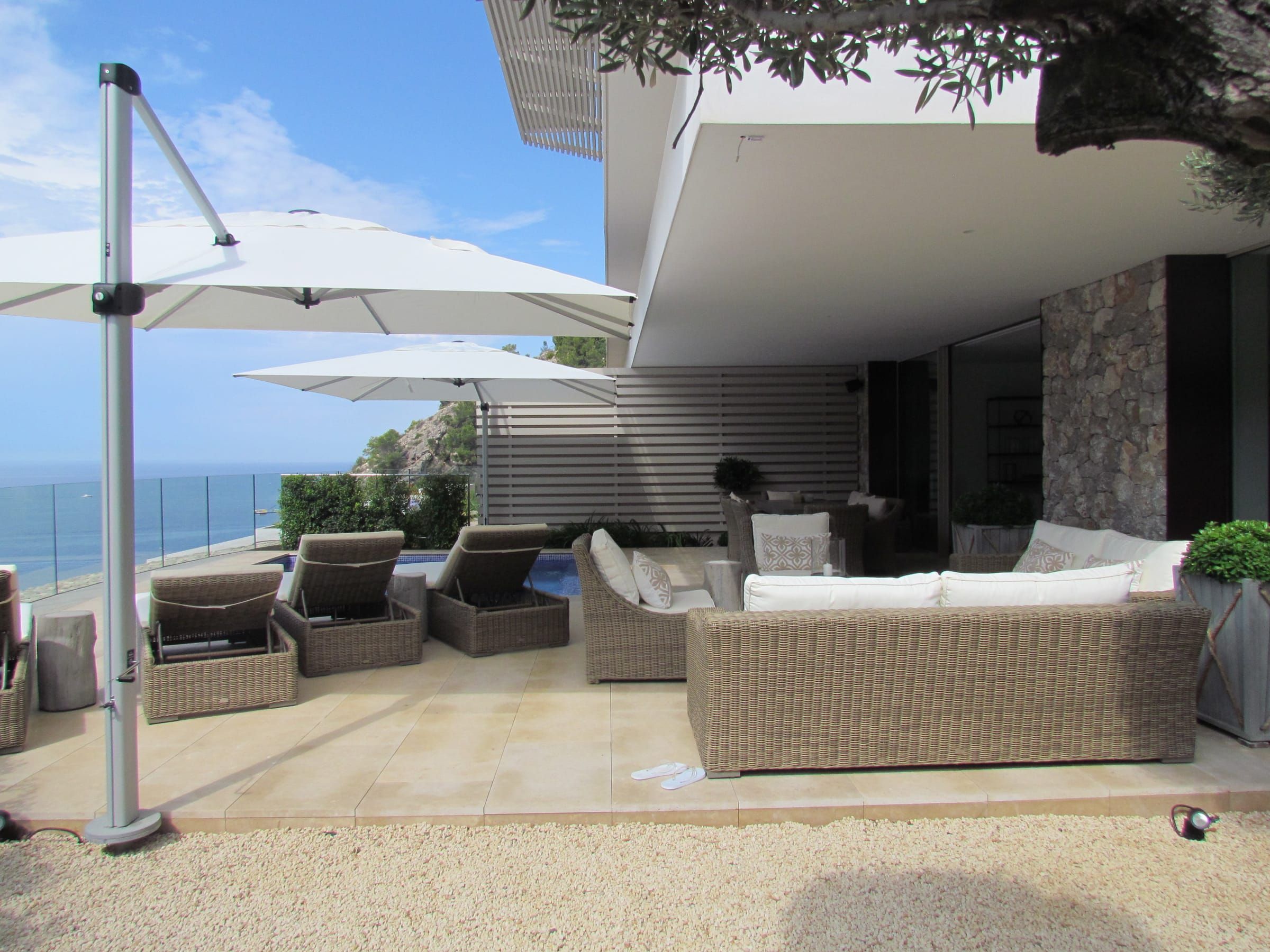 Terrace with parasols, sun loungers and wicker sofas next to the house
