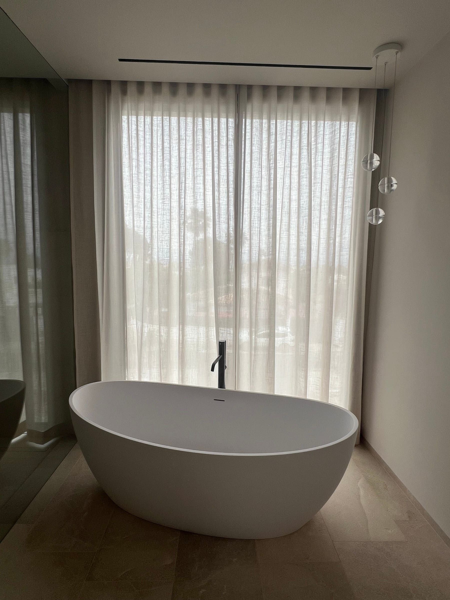 Baño con bañera exenta frente a cortinas de visillo blanco