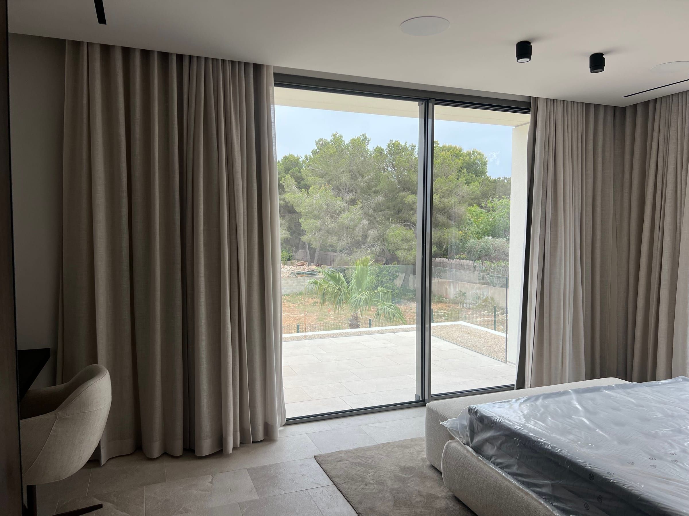 Dormitorio con cortinas en tono topo enmarcando las puertas correderas a la terraza