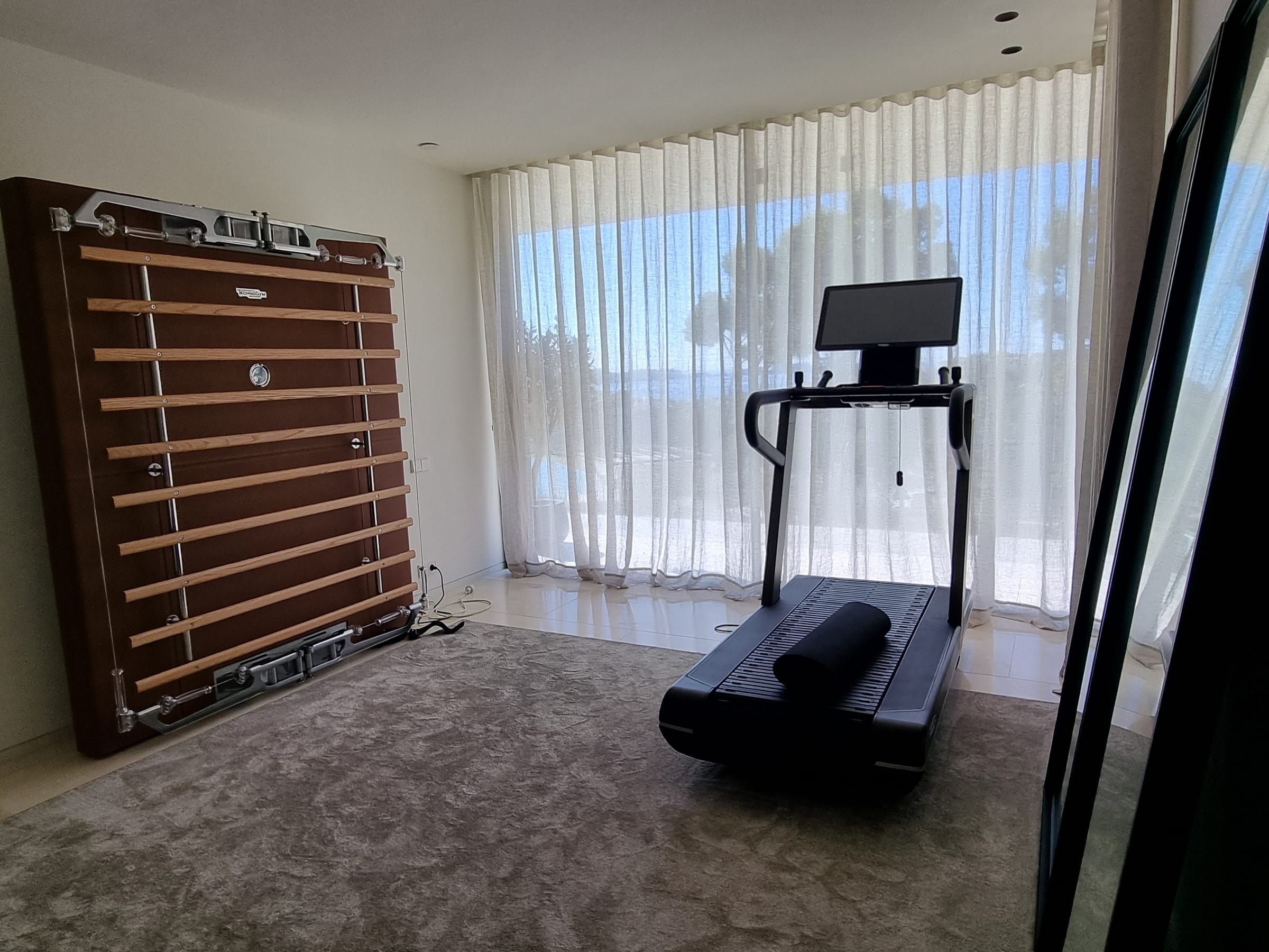 Fitnessraum mit Wellenvorhängen und Blick auf die Pinien