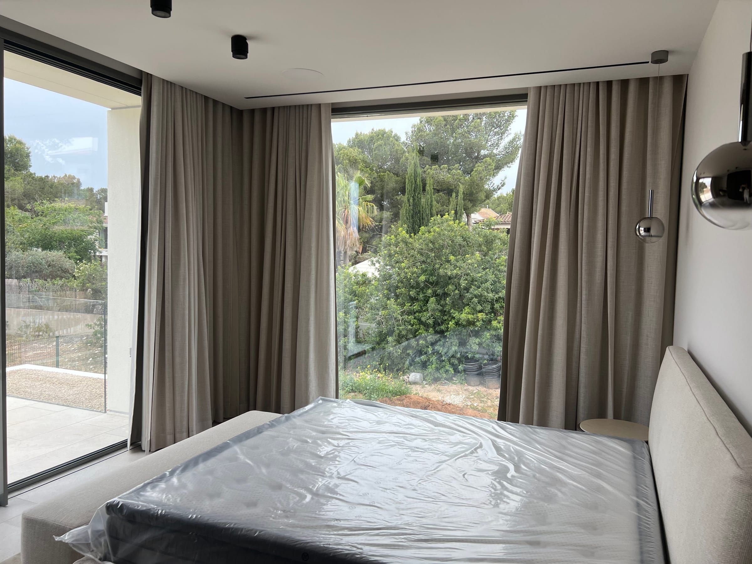 Dormitorio con cortinas en tono topo en dos ventanales con vistas al jardín