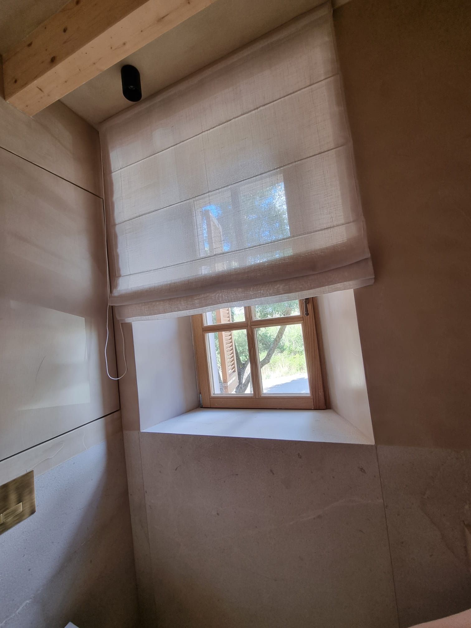 Light-coloured Roman blind over a small window with a wooden frame