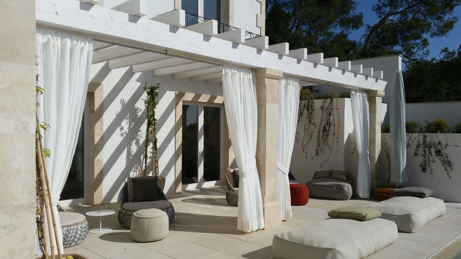 Weiße Pergola mit Außenvorhängen über einem Lounge-Bereich mit Bodenkissen